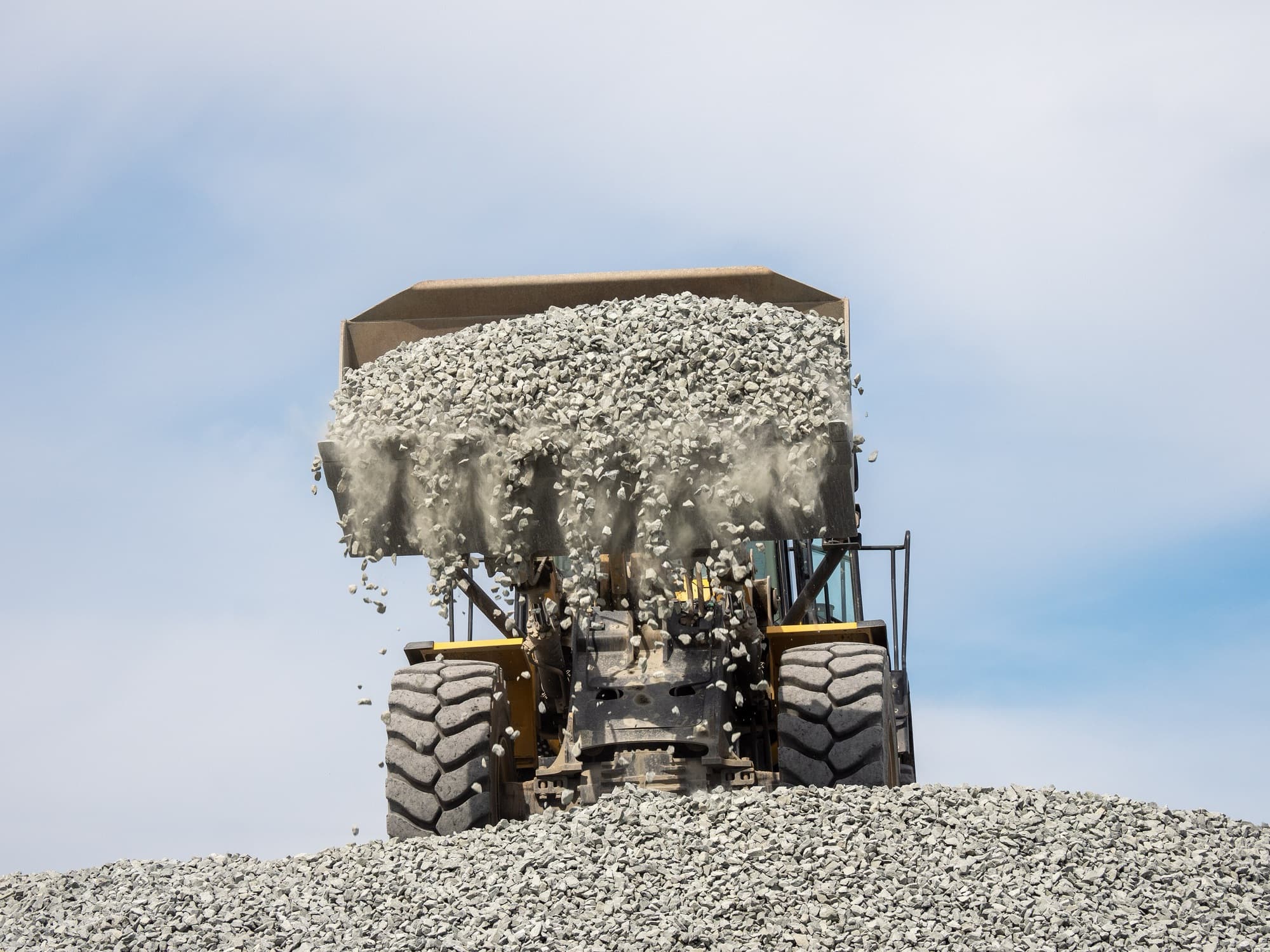 A wheel loader at work, tipping a full bucket of crushed stone onto a stockpile.