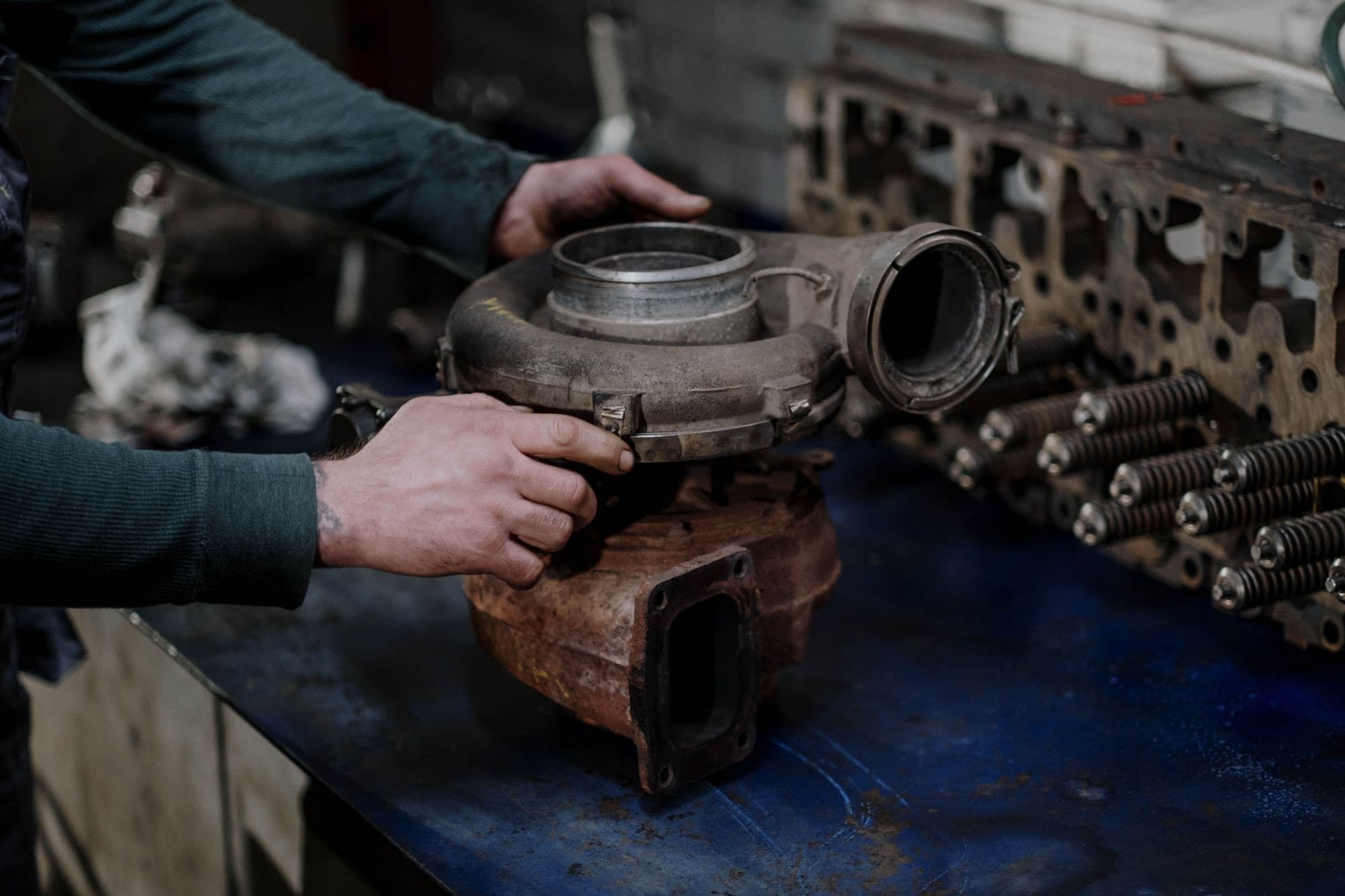 A technician holds an old diesel turbocharger on a workbench beside a cylinder head.