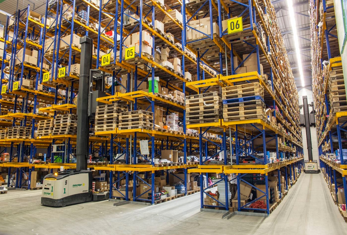 Warehouse aisle with tall pallet racking stocked with boxed parts.