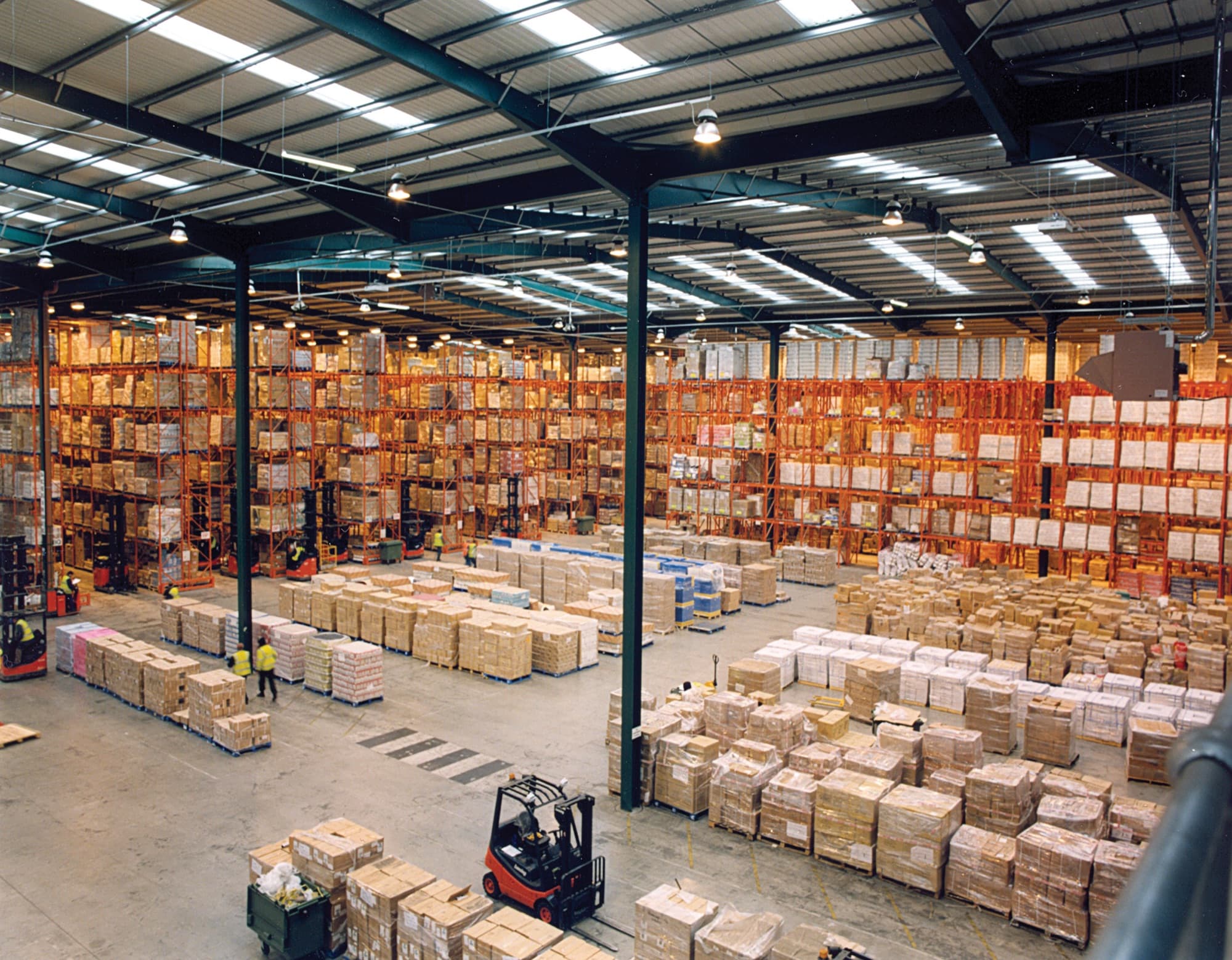 A large warehouse with high pallet racks, a forklift and shrink-wrapped pallets.