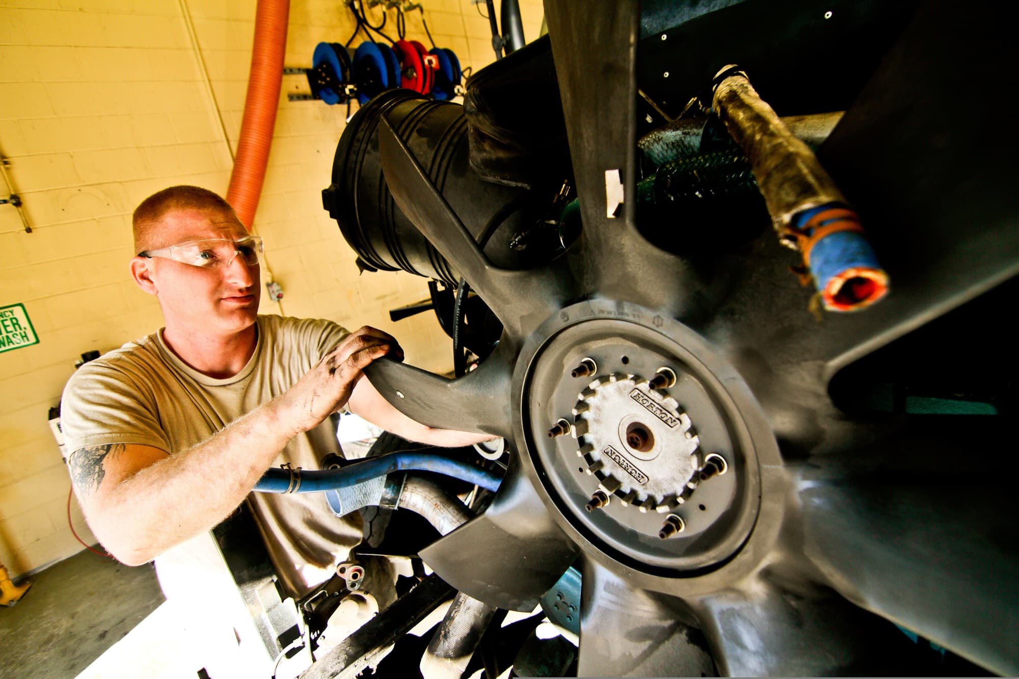 A mechanic in safety glasses works on the engine of a heavy truck in a workshop.